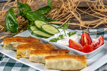 Spinach pie in a white plate served with garniture,tomato and cucumber with a glass of tea.
