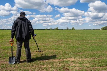 Treasure hunter. Man with metal detector. Human search treasure on green field. Guy with metal detector and shovel. Treasure hunter with his back to camera. Concept of archaeological excavations
