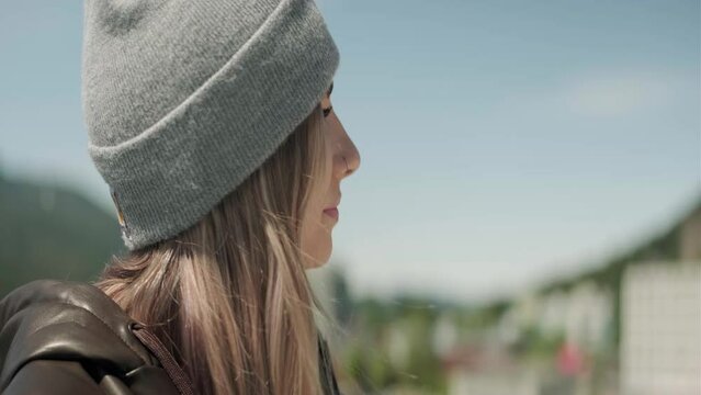 Blonde young woman wearing a beenie sipping a drink on a cruiseship outdoors traveling through Alaska. Close Up. Right Face Angle. Anamorphic