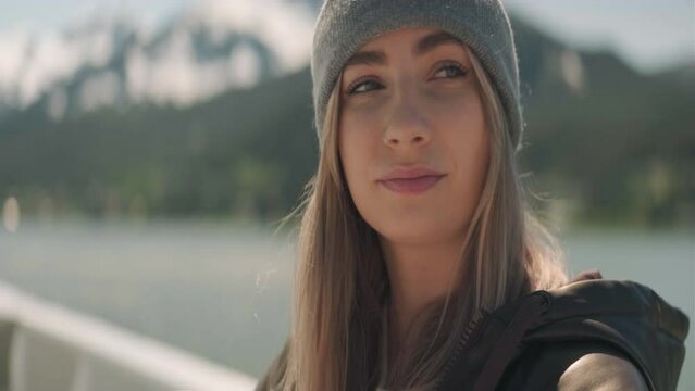 Blond young woman wearing a beenie sipping a drink outside on a cruiseship traveling  through Alaska. Close Up. Left Face angle. Anamorphic