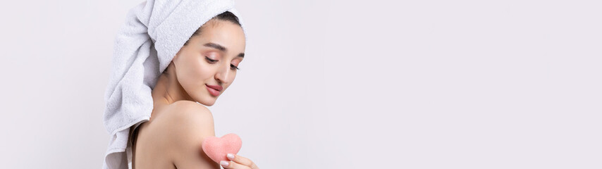 Fototapeta na wymiar Beautiful girl with thick eyebrows and perfect skin at white background, towel on head, beauty photo. Holding a cosmetic pink heart sponge.