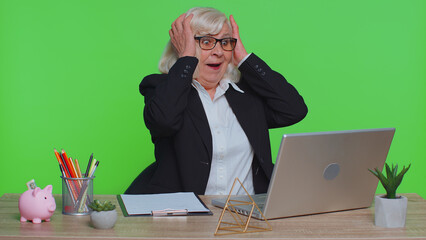 Senior business office woman freelancer wears glasses using laptop computer, analyzes financial charts celebrate success win scream rejoices doing winner hands gesture say Yes sits at workplace desk