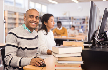 Portrait of adult Hispanic man looking at camera with smile while working on computer in library