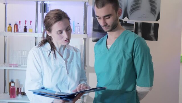 Two attentive doctors women and men in medical apparel held clip-folders and discussed ultrasound pictures. Lifestyle outdoor scene