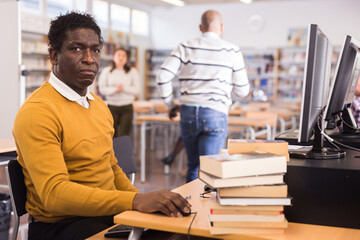 Portrait of positive young adult man studying in computer class at library