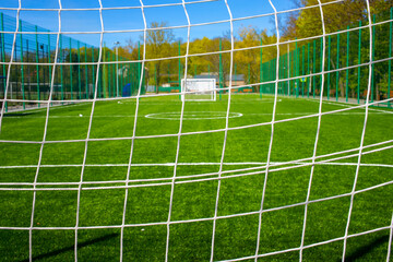 Look through net to football field in soccer stadium. Soccer field with green grass in football sport stadium behind net curtain. Sport equipment, football gate. Selective soft focus.
