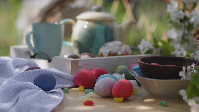 Easter brunch outdoor. Colorful eggs, bean-shaped lollipops, blossoming cherry branches on a wooden table