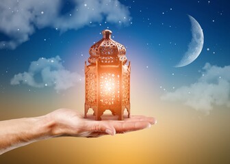 Ornamental Arabic Muslim  lantern with burning candle glowing in hand on night background