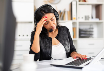 Obraz premium Weary latin woman wearing microphone headset feeling stress from work in office. Overwork concept