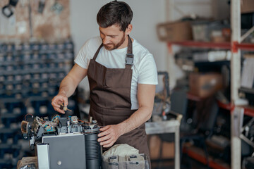 Repairman in uniform checking coffee machine in own workshop