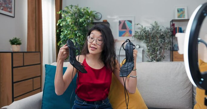Girl sitting on living room couch showing high heel shoes in front of camera. An influencer stylist showing off fashionable footwear on social media. Opinion sets seasonal trends.