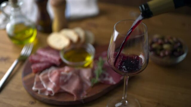 pouring red wine into glass with italian antipasto plate background
