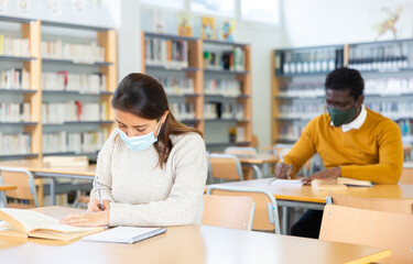 Portrait of young adult woman wearing mask for viral protection studying in at public library