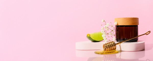 Jar of cosmetic cream, piece of lime and honey on pink background with space for text