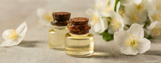 Obraz na płótnie Canvas Bottles of essential oil and jasmine flowers on light background, closeup