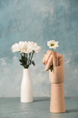 Wooden hand with chrysanthemum flower on blue background
