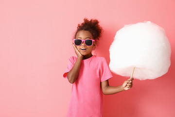 Little African-American girl with cotton candy on pink background
