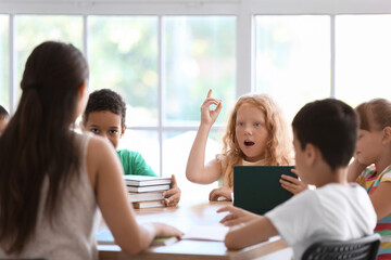 Little redhead girl asking question during literature lesson in classroom