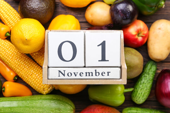 Different fresh fruits, vegetables and cube calendar with date NOVEMBER 1 on wooden background, closeup. World Vegan Day concept