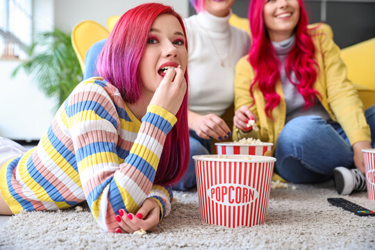 Beautiful woman eating popcorn while watching movie with her friends at home