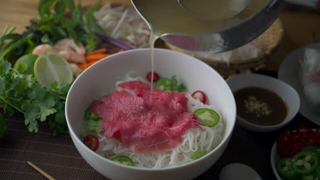 pouring soup into authentic vietnamese pho rice noodle with raw beef