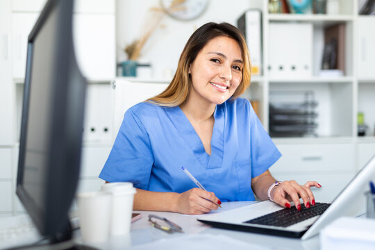 Young hispanic woman doctor assistant working in medical office using laptop computer