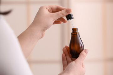 Woman holding bottle of serum at home, closeup
