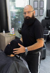 scene of a barber looking at the camera while hold the head of a man with his face covered by a towel