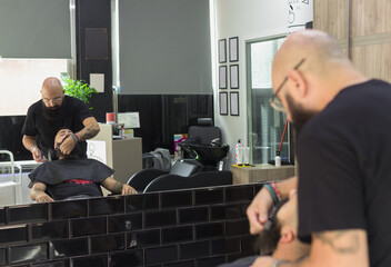 scene reflected on a mirror of a bald barber combing the beard of his client  into a barbershop