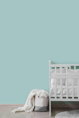 Baby crib and basket with blanket near green wall
