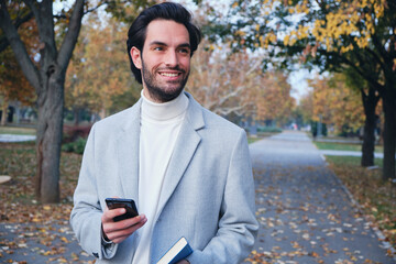 Fototapeta premium Young handsome businessman enjoying his free time outside on a beautiful autumn day, texting on his phone