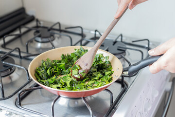 Hands cooking ora-pro-nobis (Pereskia aculeata) in a frying pan, a popular edible plant in Brazil