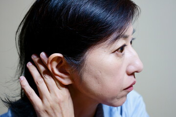 耳元に手をやる中年女性の横顔　白髪　難聴
