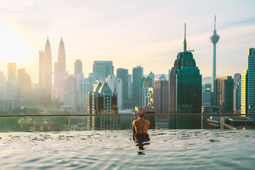 Aziatische zakenman ontspant in het zwembad op het dak achter het prachtige uitzicht op de stad Kuala Lumpur in de zonsopganghemel, Maleisië