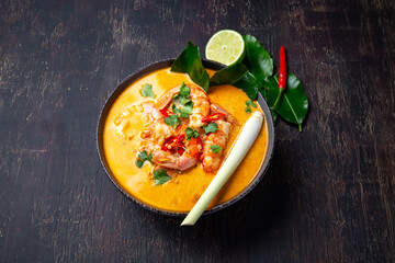 Shrimps Tom Yam Kung in grey bowl with thai spices on autentic tray top view, wooden background.