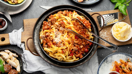 Assortment of Italian pasta with traditional sauces for dinner on dark background. Homemade food concept