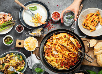 Assortment of Italian pasta with traditional sauces for dinner on dark background. Homemade food concept