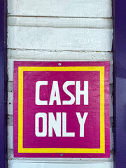 Colourful cash only sign on wooden white textured wall in front of a store.