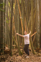 A Caucasian man hugging a bamboo forest wearing informal clothes. 