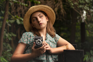 Artistic Portrait of a little girl holding a vintage camera, wearing a green dress and a straw hat. 