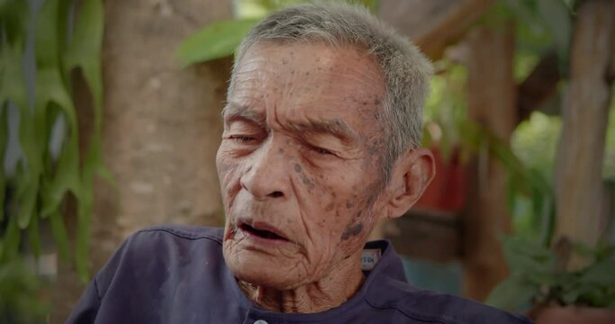 Asian male farmer who is the long life native 98 years, white hair, freckled skin, still in good health living in a rural farmer's village, talking about his story with visitors.
