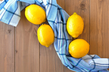 three fresh lemons on a wooden table. there is a cotton kitchen towel next to it
