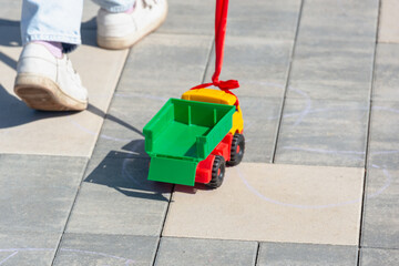 The child rolls a toy car on a rope behind him.