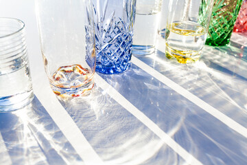 Light through collection of colourful water glasses in sunlight