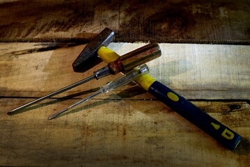A hammer and two screwdrivers on an old board.