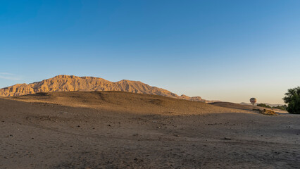 Fototapeta na wymiar Morning in the desert. A bright balloon rises above the sand dunes. Shadows on the sand. A picturesque mountain range, illuminated by the sun, against a clear blue sky. Egypt. Luxor