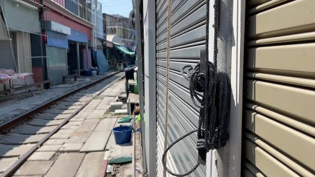 Rope cord hanging on wall pulls outdoor umbrella at local Maeklong market (Talad Rom Hub), popular tourist destination. Train track on ground - day   