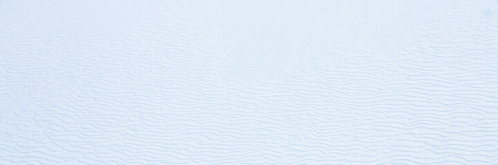 Beautiful winter background with snowy ground. Natural snow texture. Wind sculpted patterns on snow surface. Wide panoramic texture for background and design.