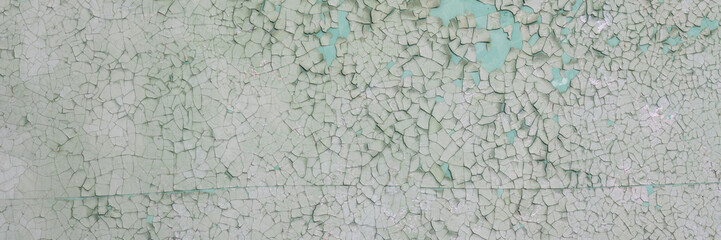 Peeling paint on the wall. Panorama of a concrete wall with old cracked flaking paint. Weathered rough painted surface with patterns of cracks and peeling. Wide panoramic grungy texture for background