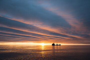 Amazing summer seascape. Cargo ship at sea in the Arctic. Delivery of goods along the Northern Sea Route. Chukchi Sea, Arctic Ocean, Russia. Beautiful sunrise. Bright summer nights in the polar region